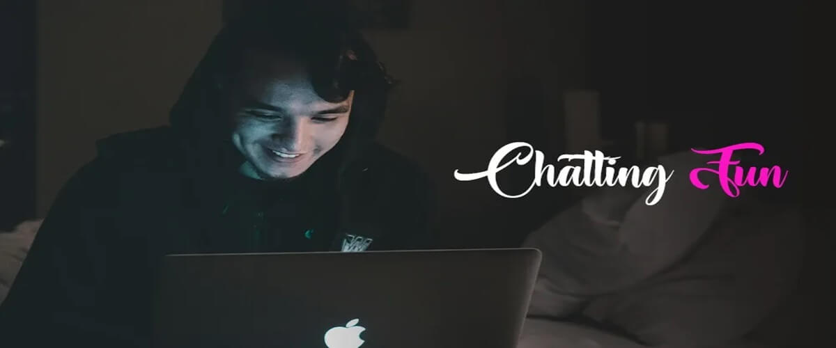 Man sitting in a dark room with a hoodie on and smiling while chatting